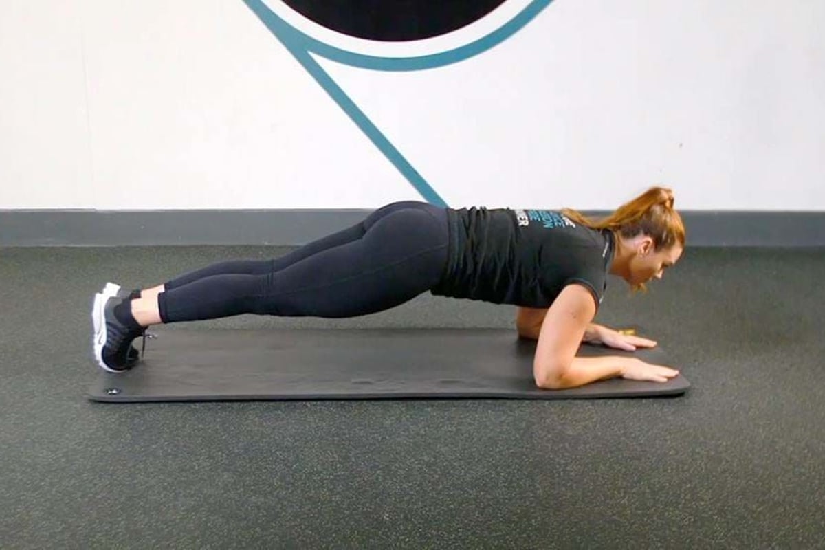 Woman in black sportswear holding a plank position on a mat in a gym