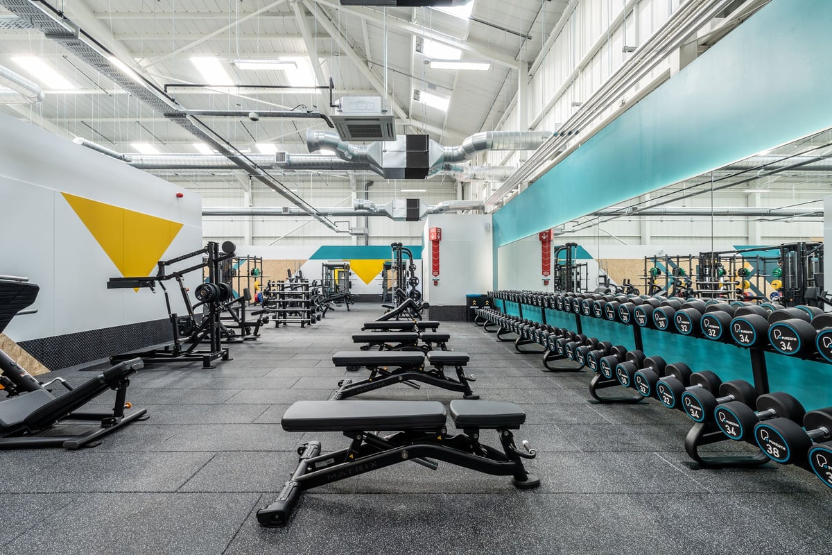PureGym Keighley: Weight benches, squat racks, free weights, rubberized flooring in a colourful gym interior.