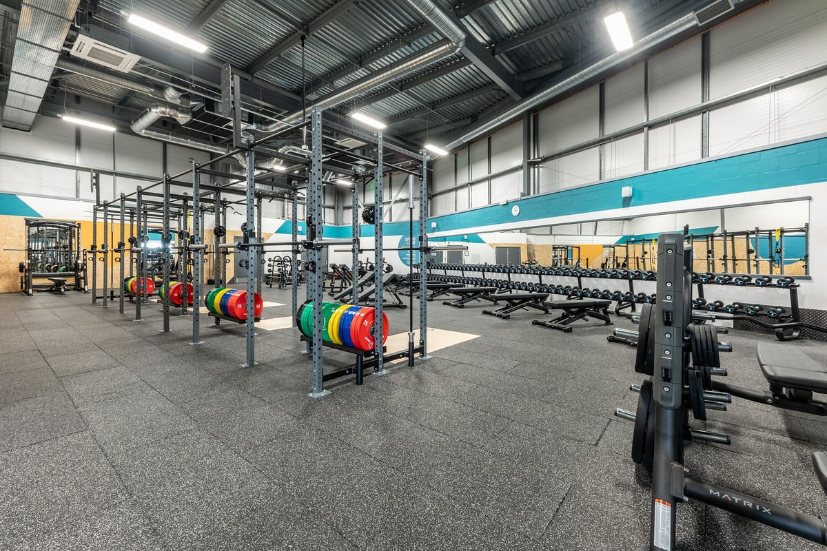 PureGym Tamworth: Racks of free weights, colourful weight plates, benches, and rubberised flooring in a gym studio.