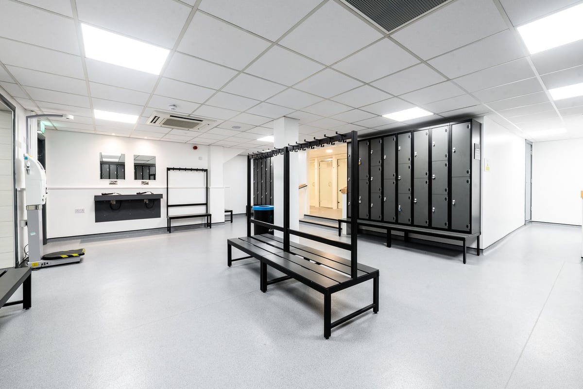 PureGym Manchester Moston: Locker room with benches, lockers, and basic amenities.
