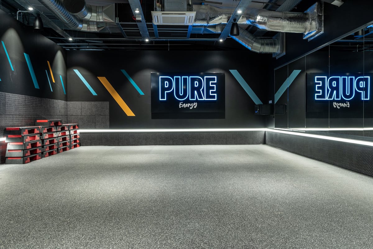 PureGym Glasgow Rutherglen: Gym studio with neon signage, ventilation ducts, mirrored walls, and rubberized flooring.