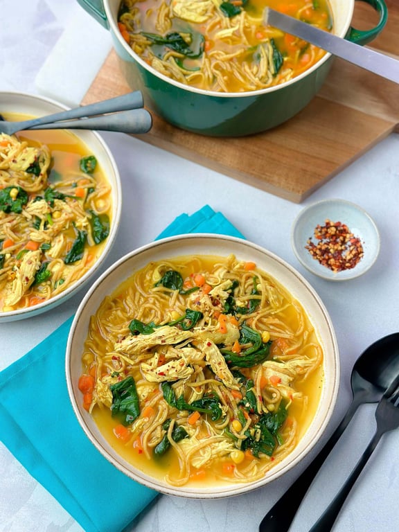Bowls of chicken noodle soup with spinach and diced carrots on a table