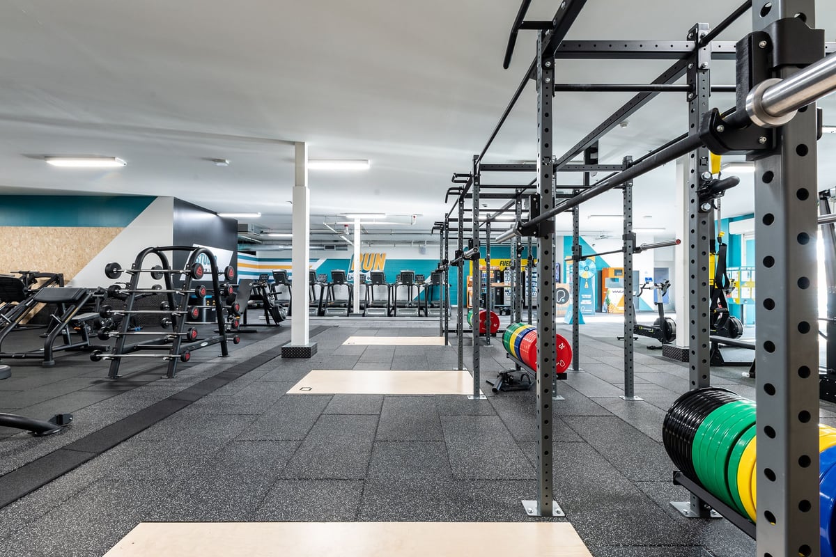 PureGym Ashton Under Lyne: Fitness rig, squat racks, weight plates, cardio machines, and rubberized flooring in a gym studio.