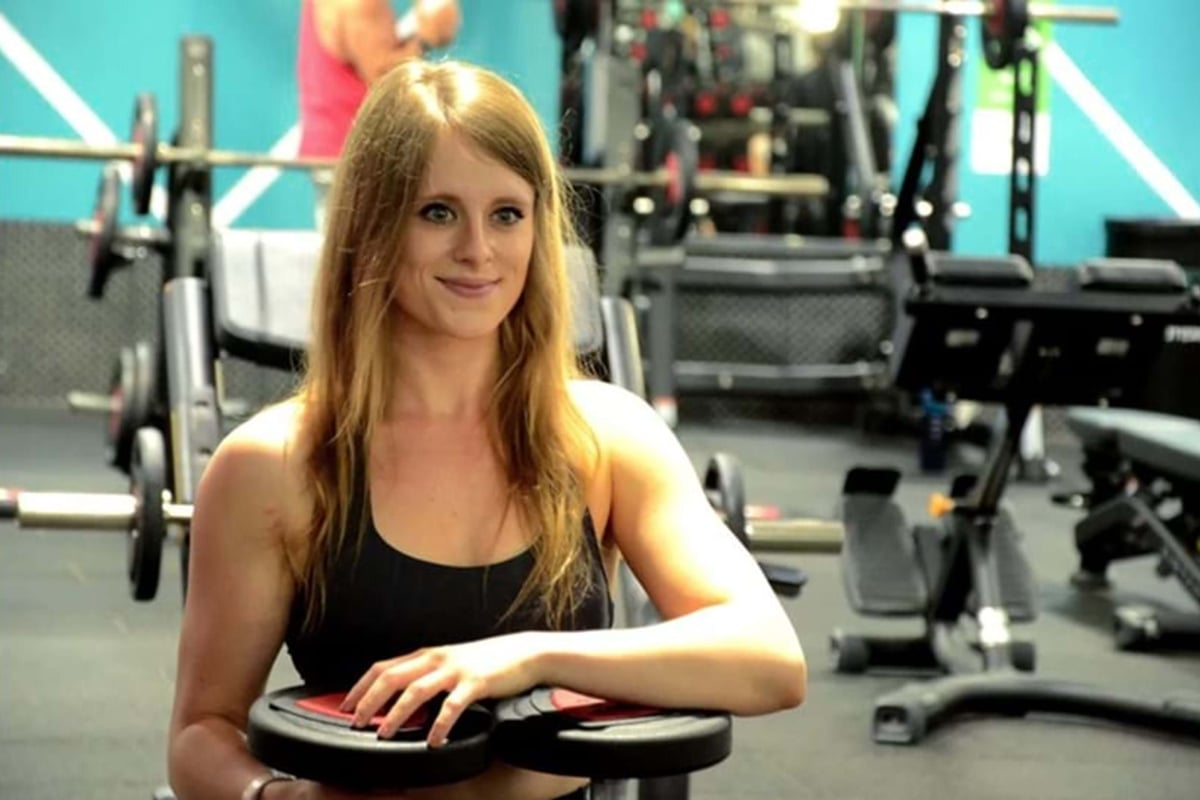 Woman in black sportswear holding weight plates in gym with exercise equipment behind her