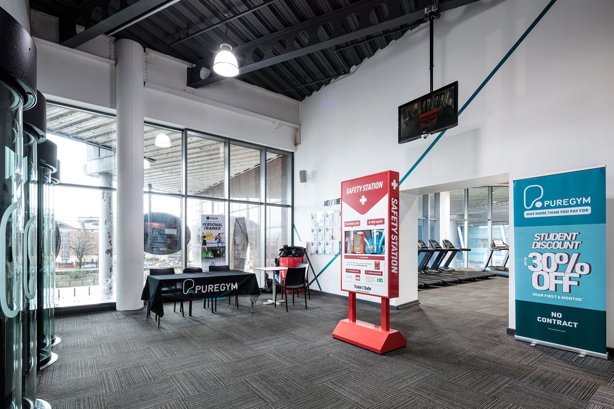 PureGym Cardiff Central: The gym interior has cardio machines, weight racks, and promotional stands.