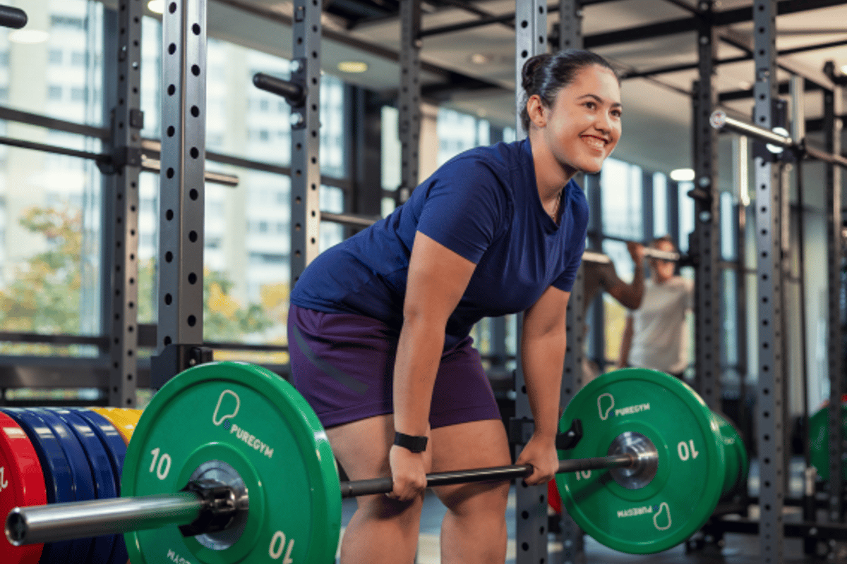 Frau führt Kreuzheben mit grünen Gewichtsscheiben an einer Langhantel in einem Fitnessstud