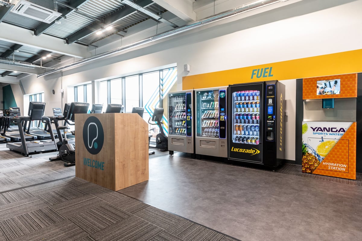 PureGym Bicester: Vending machines, fitness equipment logo on wood, patterned flooring.