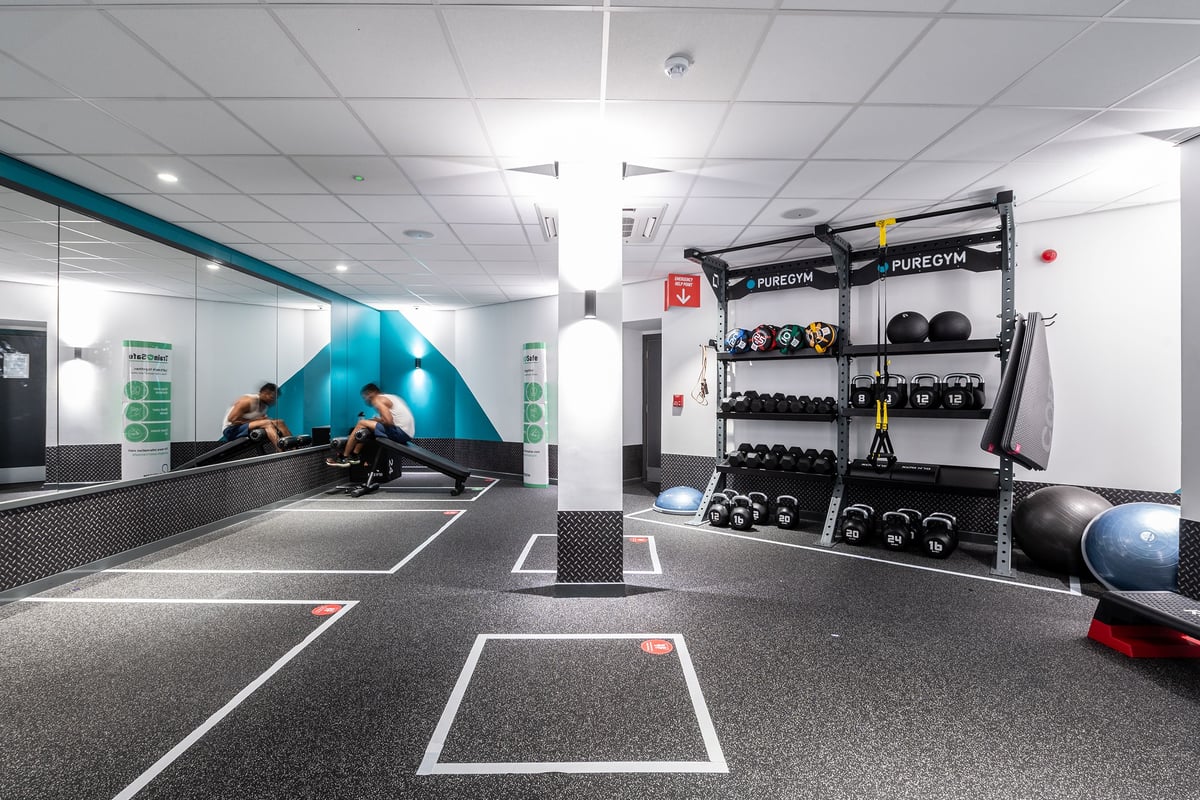 PureGym London Sydenham: Rubberized flooring, weight racks, punching bags, and a climbing wall inside a gym studio.