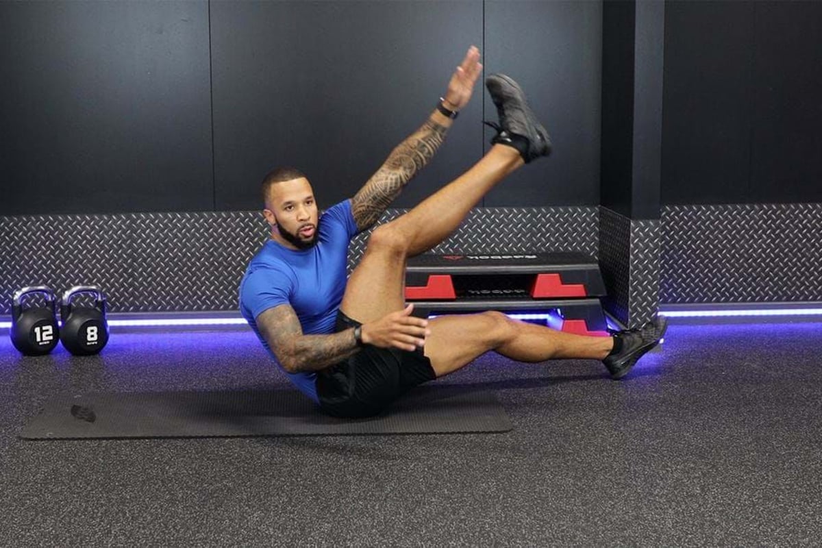 Man in blue shirt doing a seated leg raise exercise on a gym mat