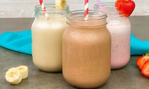 Three jars of banana, chocolate, and strawberry milkshakes with fruit garnishes and stripe