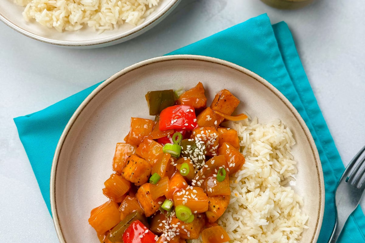 Two plates of sweet and sour tofu with rice, garnished with spring onions and sesame seeds
