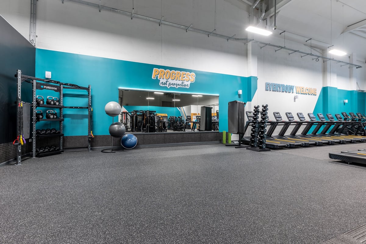 PureGym Lincoln Carlton Centre: Racks, free weights, medicine balls, rubberized flooring in a teal and grey gym interior.