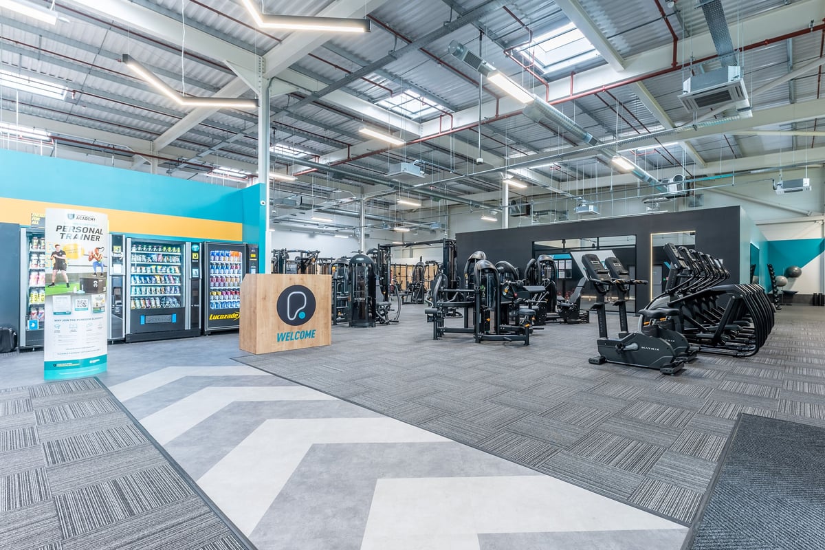PureGym Nottingham Colwick: Cardio machines, weight racks, rubberized flooring in a gym setting with vending kiosks.