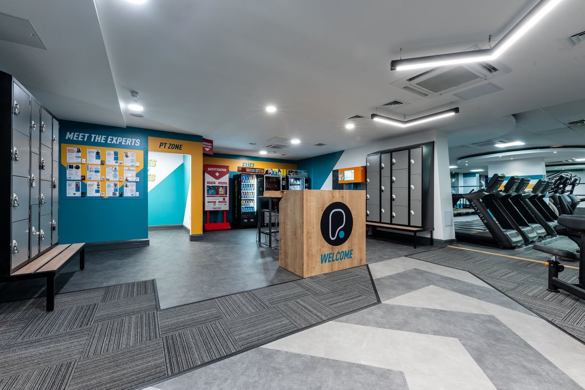 PureGym London Edgware: Gym reception area with cardio machines, self-service kiosks, treadmills, and rubberised flooring.
