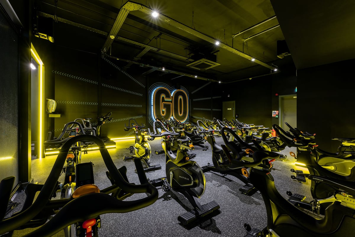 PureGym Solihull Sears Retail Park: Rows of stationary bikes, dim lighting, and neon "GO" signage in a gym cycling studio.