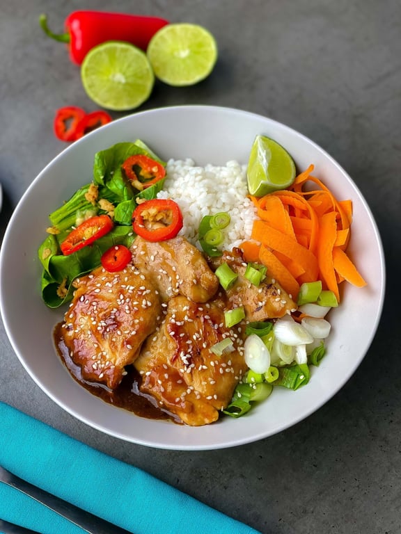 Chicken with sesame seeds, rice, carrot ribbons, greens, spring onions, and lime wedge in
