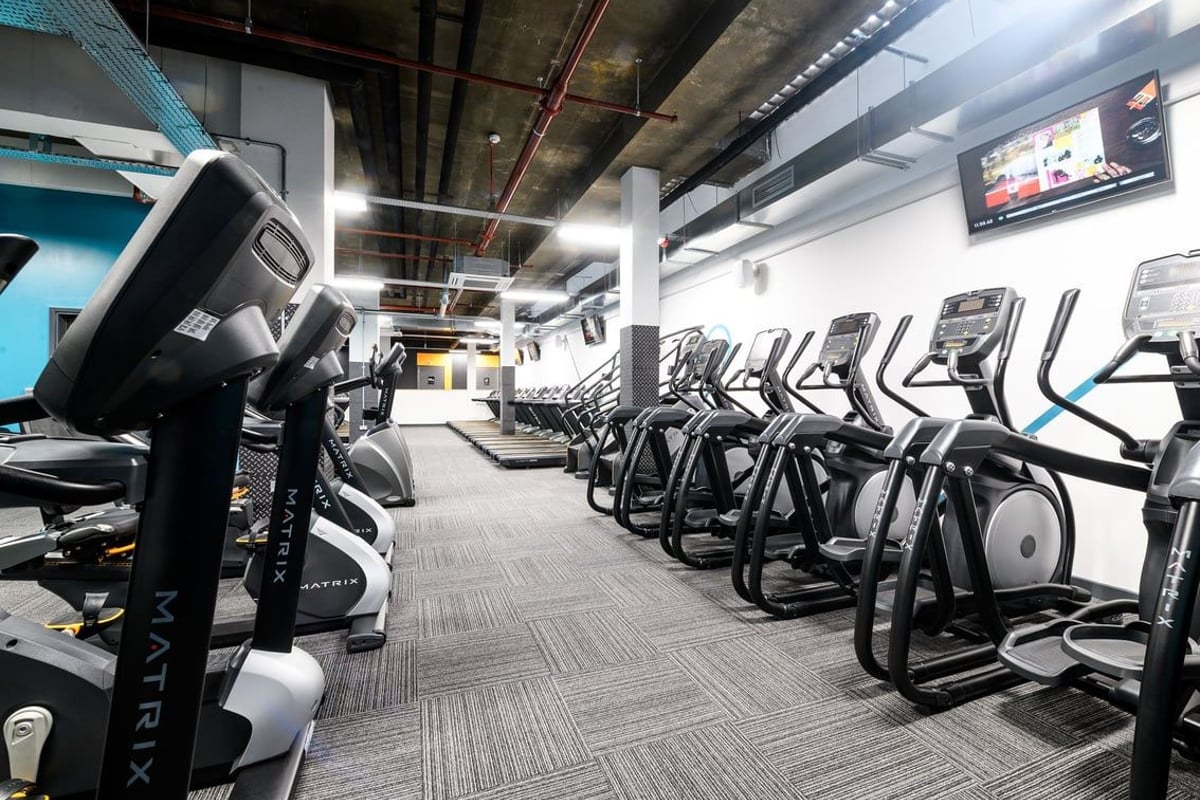 PureGym London Tottenham Court Road: Rows of modern cardio equipment in a dimly lit gym with exposed ceiling and TV monitors.