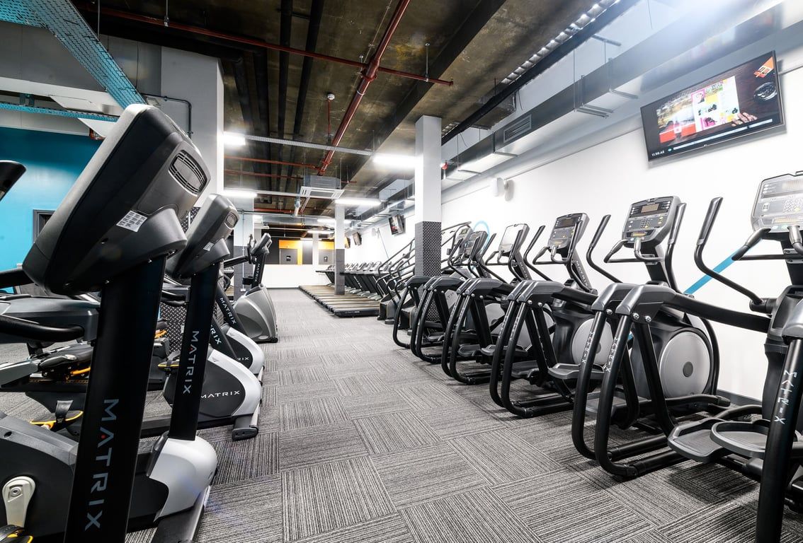 PureGym London Tottenham Court Road: Rows of modern cardio equipment in a dimly lit gym with exposed ceiling and TV monitors.