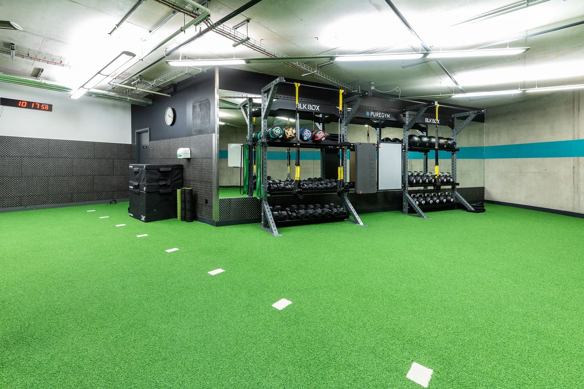 PureGym London Aldgate: Turf flooring, weight racks, dumbbells, resistance machines in an industrial-style gym area.