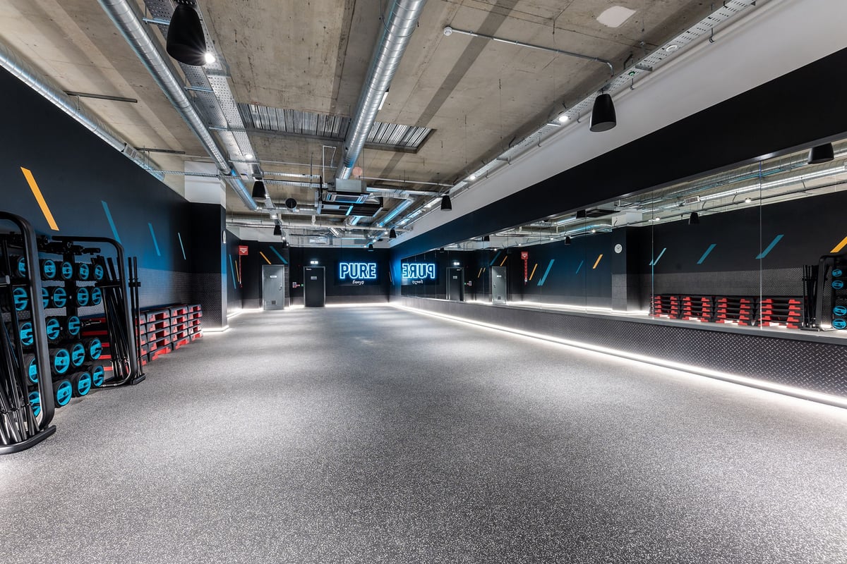 PureGym London Feltham: Rubberized flooring, sleek black walls with red accents, rows of equipment racks.