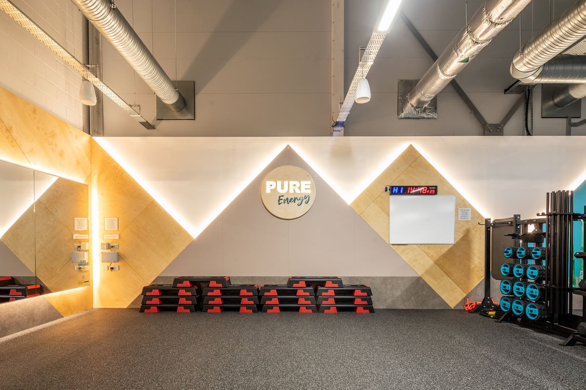 PureGym Wantage: Rows of red exercise bikes, large mirror with 'Pure Energy' logo, digital display board.