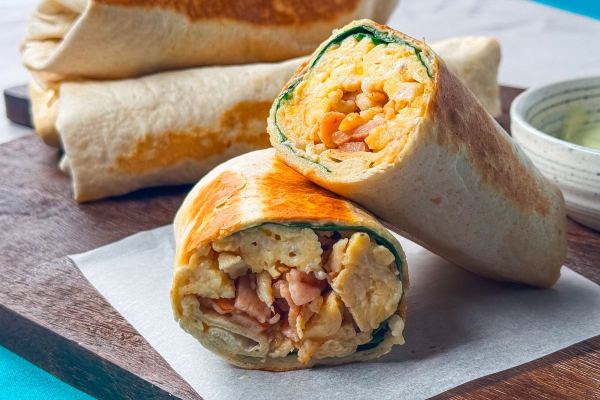 Toasted breakfast burritos filled with scrambled egg and beans on a wooden board