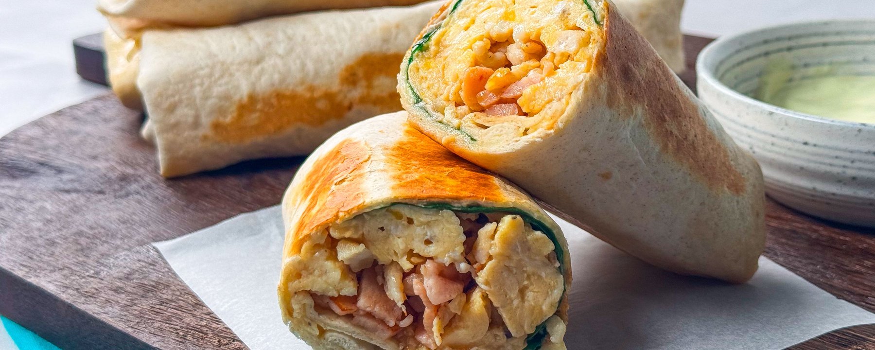 Toasted breakfast burritos filled with scrambled egg and beans on a wooden board