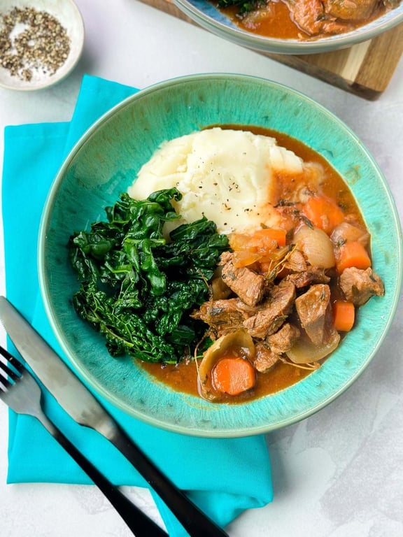 Mashed potatoes, cooked kale, and beef stew with carrots and onions in a bowl
