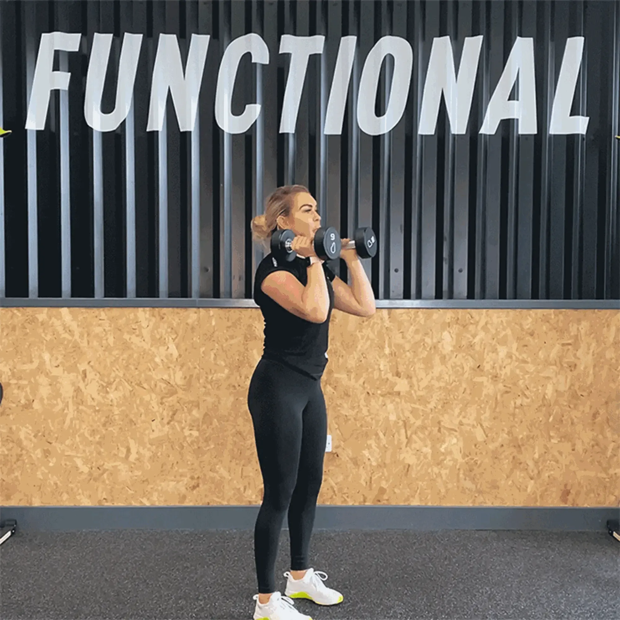 Woman lifting dumbbells in gym with functional training sign behind her