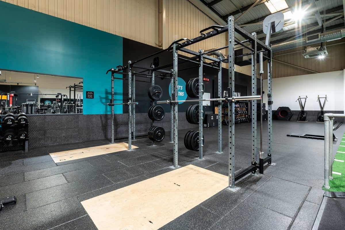 PureGym Weston-super-mare: Squat racks, weight plates, rubberized flooring, and mirrored wall in gym studio.