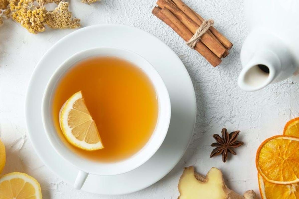Cup of tea with lemon slice, cinnamon sticks, dried orange slices, and ginger root.