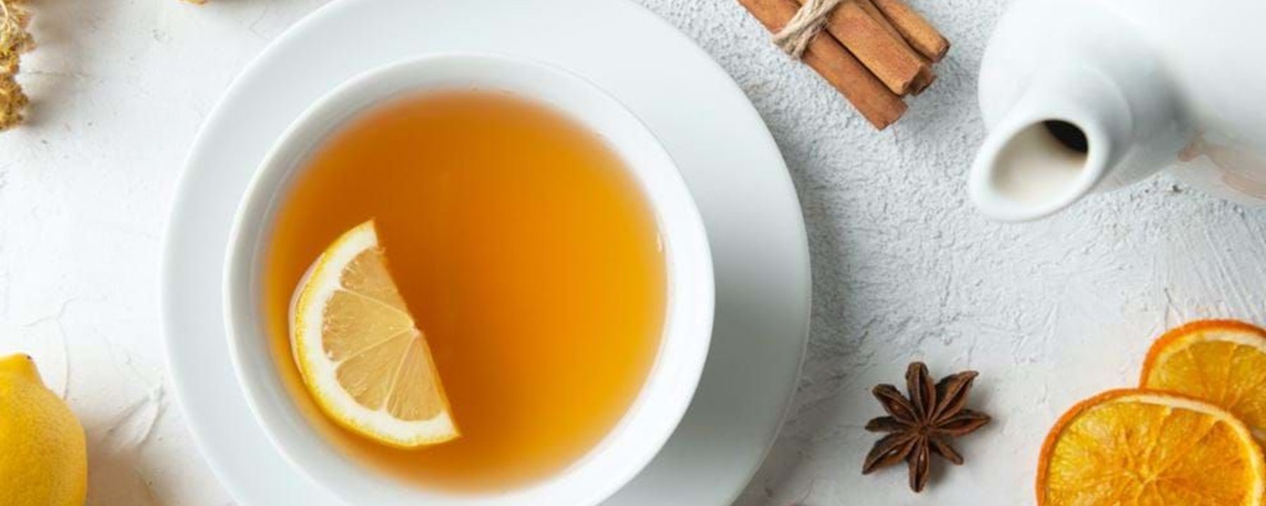 Cup of tea with lemon slice, cinnamon sticks, dried orange slices, and ginger root.