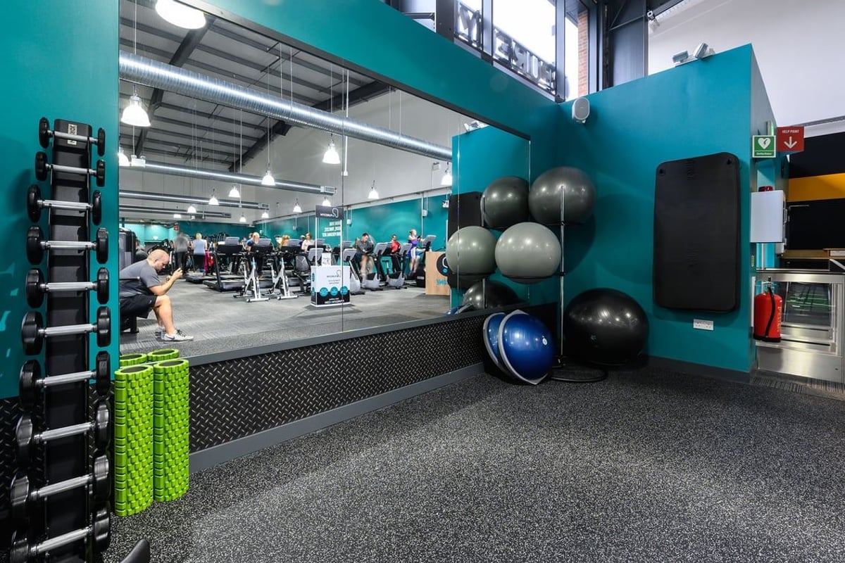 PureGym Bromsgrove Retail Park: Exercise area with weight racks, stability balls, dumbbell sets, and teal-colored walls.