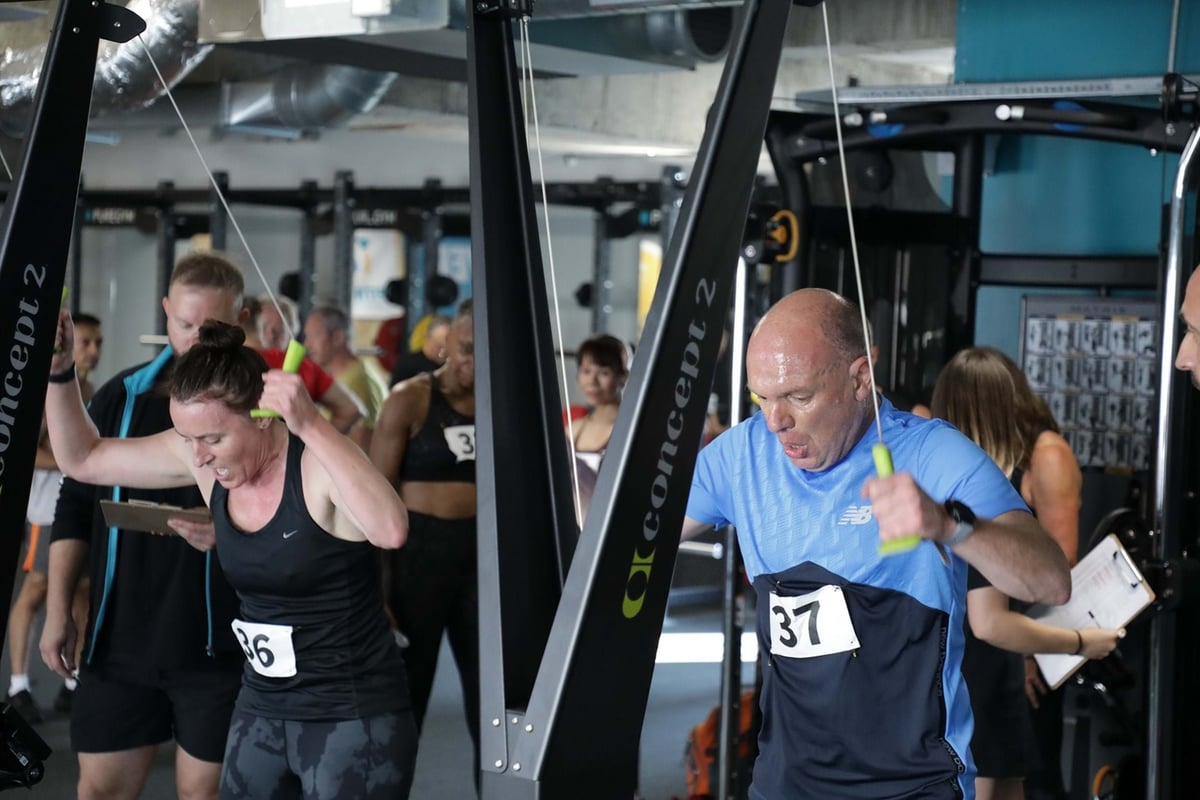 Two people intensely using Concept 2 rowing machines in a gym with others in the backgroun