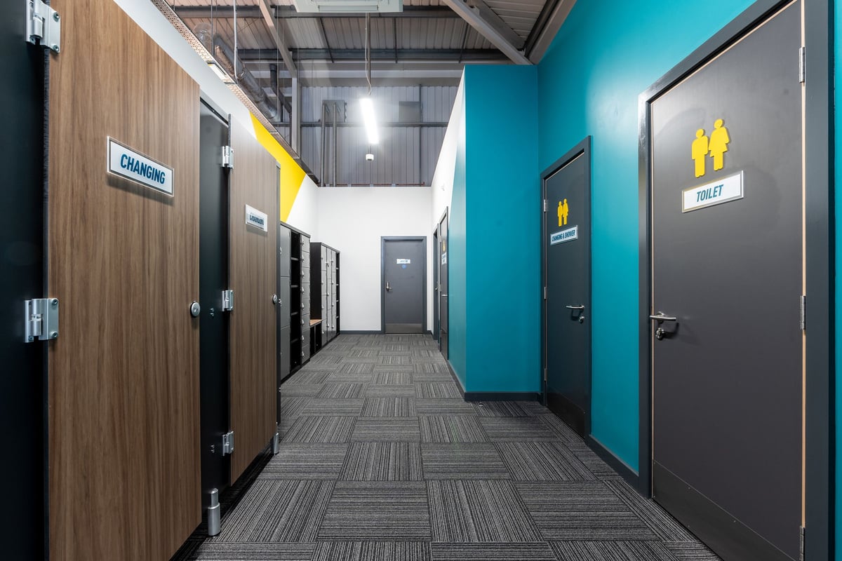 PureGym Spalding: Hallway with gender-designated restrooms, wood paneling, and tiled flooring.