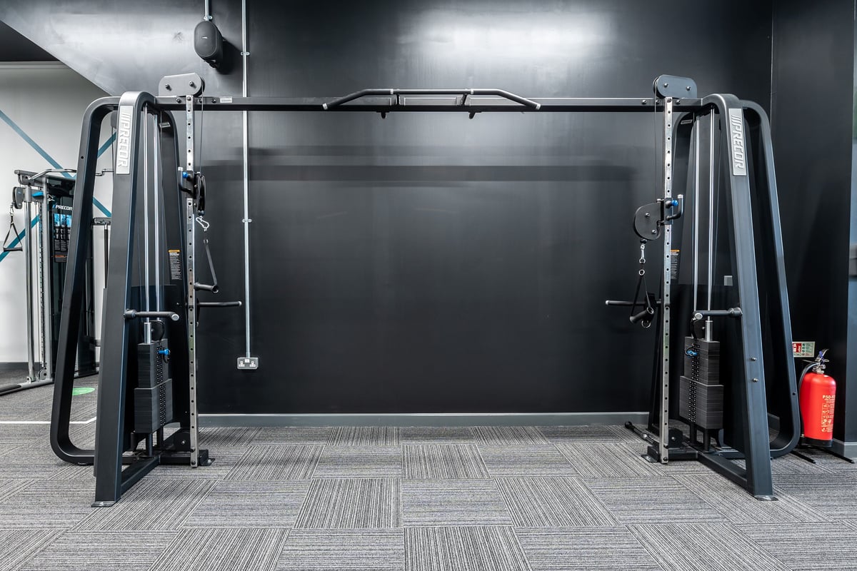 PureGym Birmingham Longbridge: Weight machines, barbell racks, padded flooring in a dimly lit gym interior.