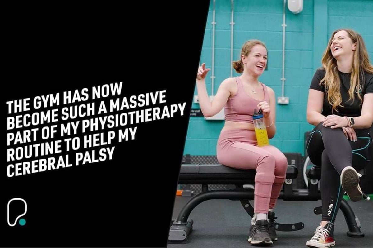 Two women in gym wear sitting on a bench laughing, one holding a water bottle.