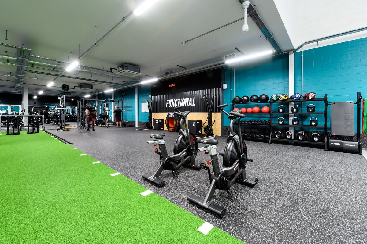 PureGym Romford: Weight benches, resistance machines, free weights, green turf area in a spacious gym setting.