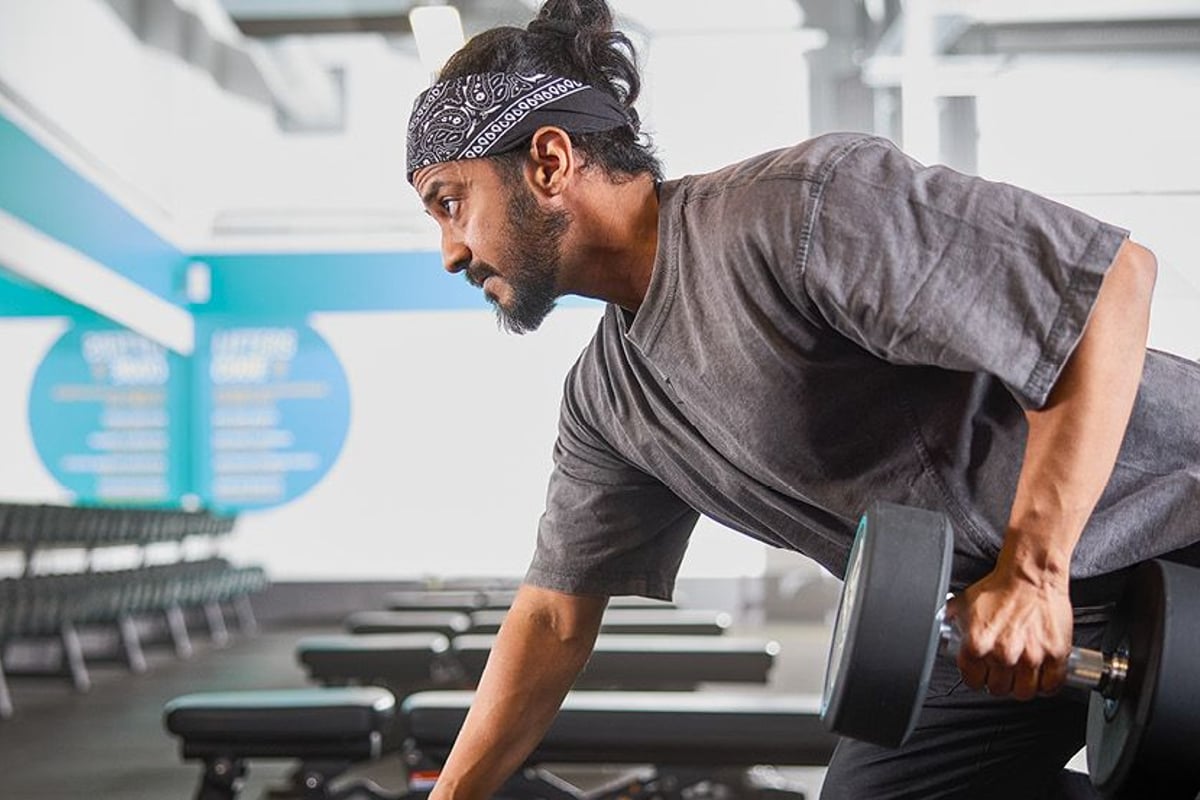 Man lifting dumbbell in gym with rows of benches and weights in background