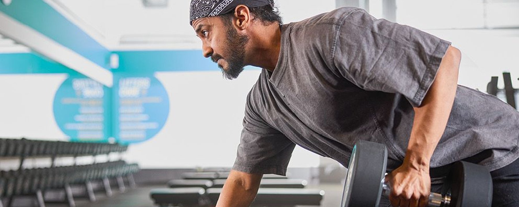 Man lifting dumbbell in gym with rows of benches and weights in background