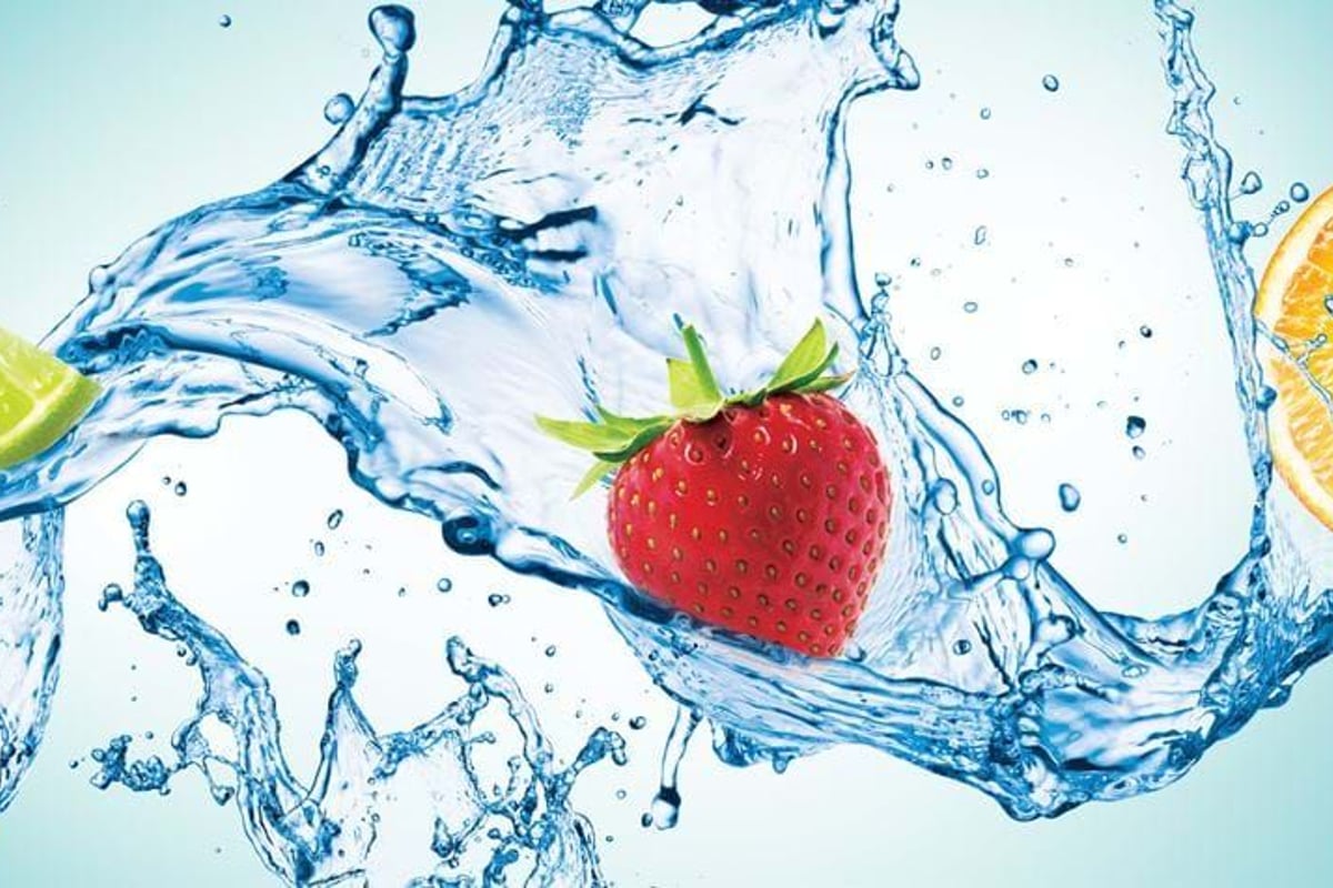 Splashing water with lime wedge, strawberry, and orange slice on blue background