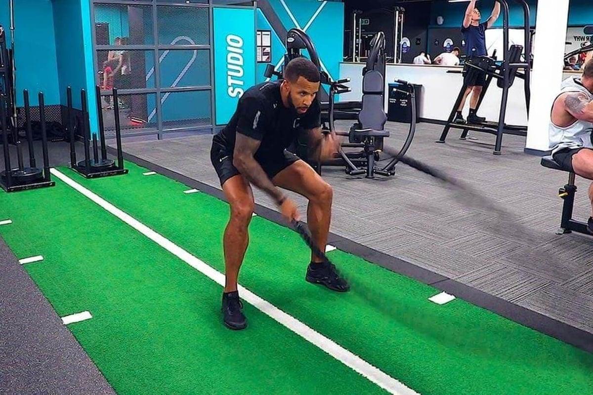 Man exercising with battle ropes on green turf in gym studio