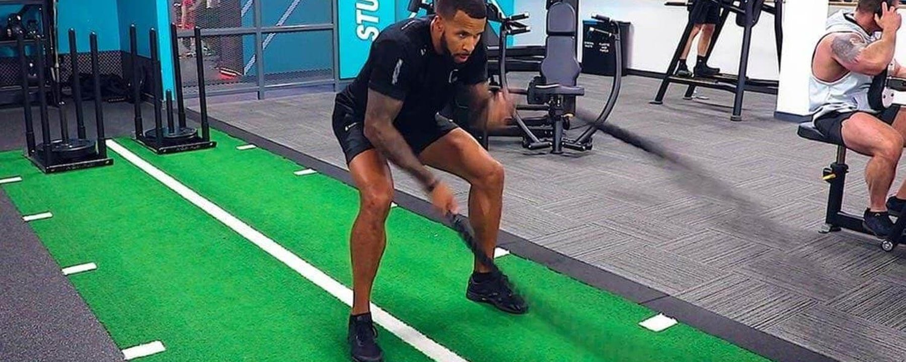 Man exercising with battle ropes on green turf in gym studio