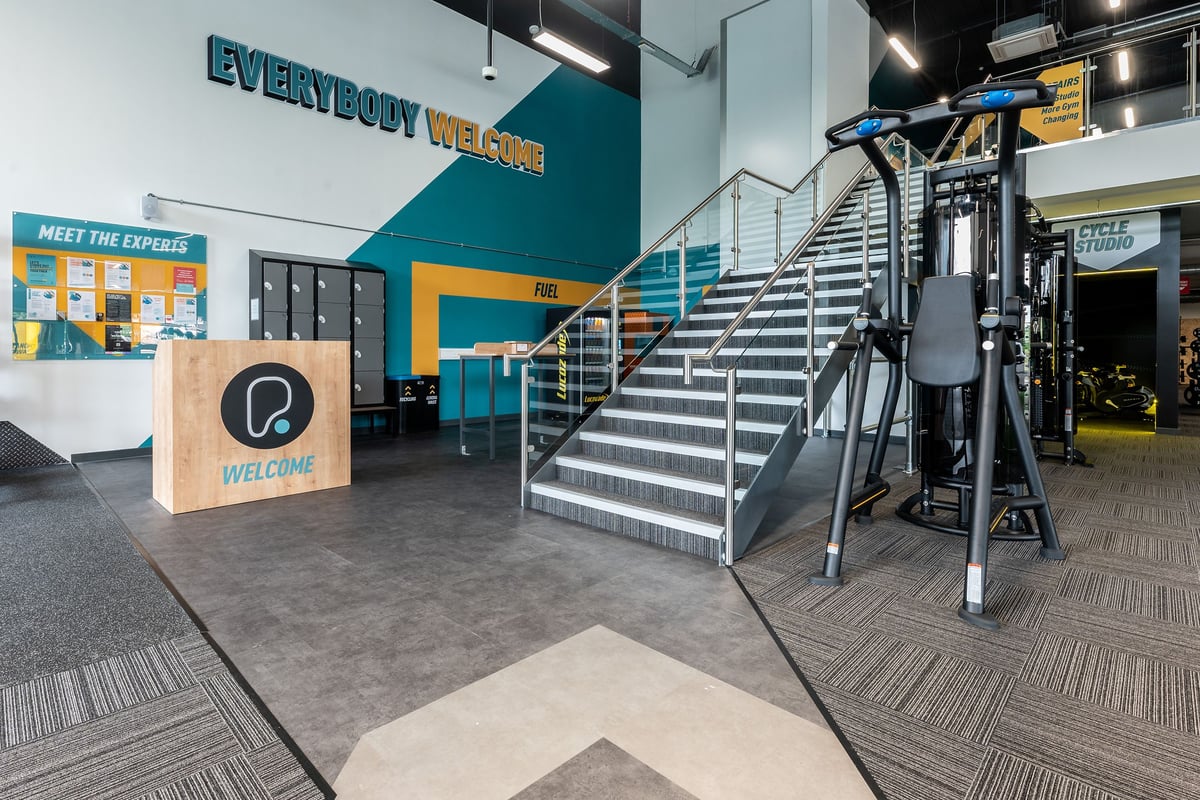 PureGym Doncaster: Metal staircases, weight plates on wall displays, and treadmills in an entrance area.