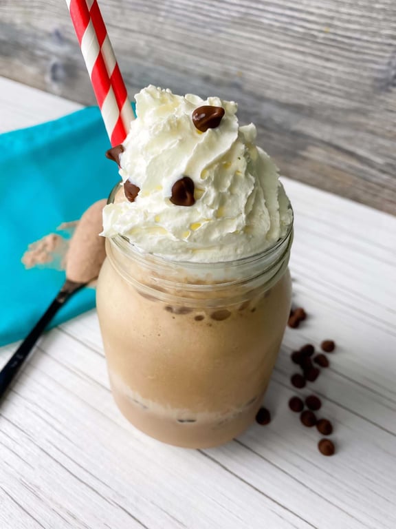 Iced coffee drink topped with whipped cream and chocolate chips in a glass jar