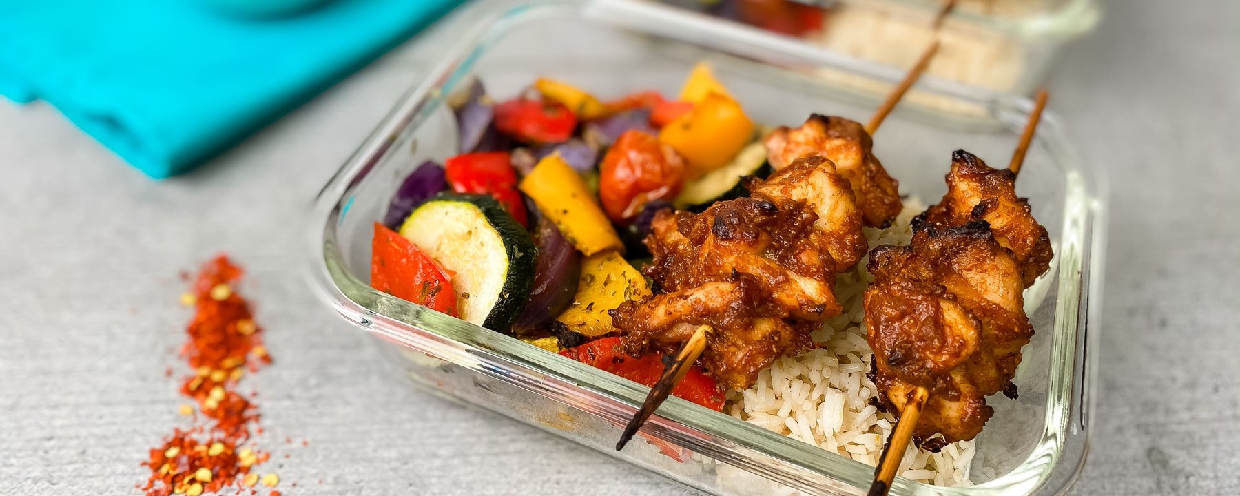 Grilled chicken skewers on rice with roasted vegetables in clear container