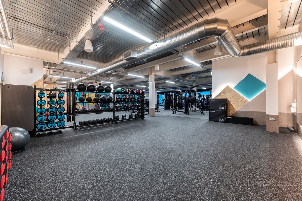 PureGym Droitwich Spa: Rows of exercise machines, weight racks, rubber flooring, and air ducts in a basement gym.