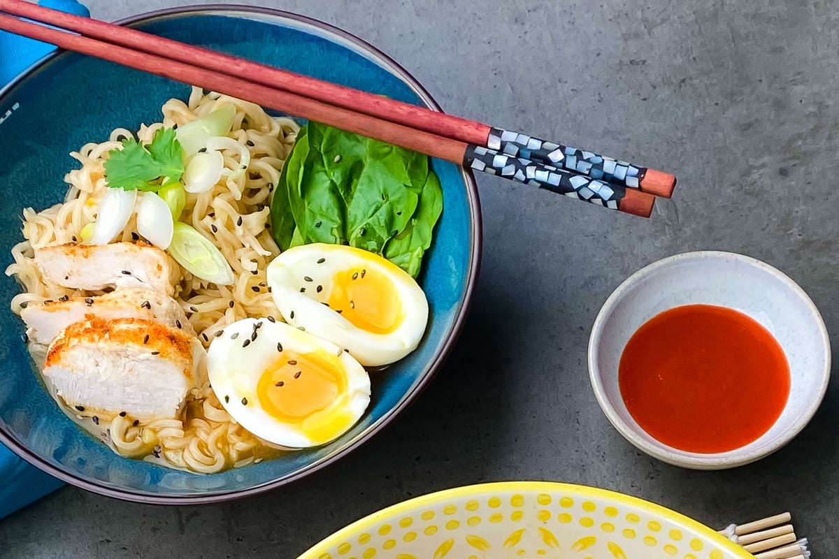 Bowl of ramen noodles topped with sliced chicken, soft-boiled eggs and green vegetables