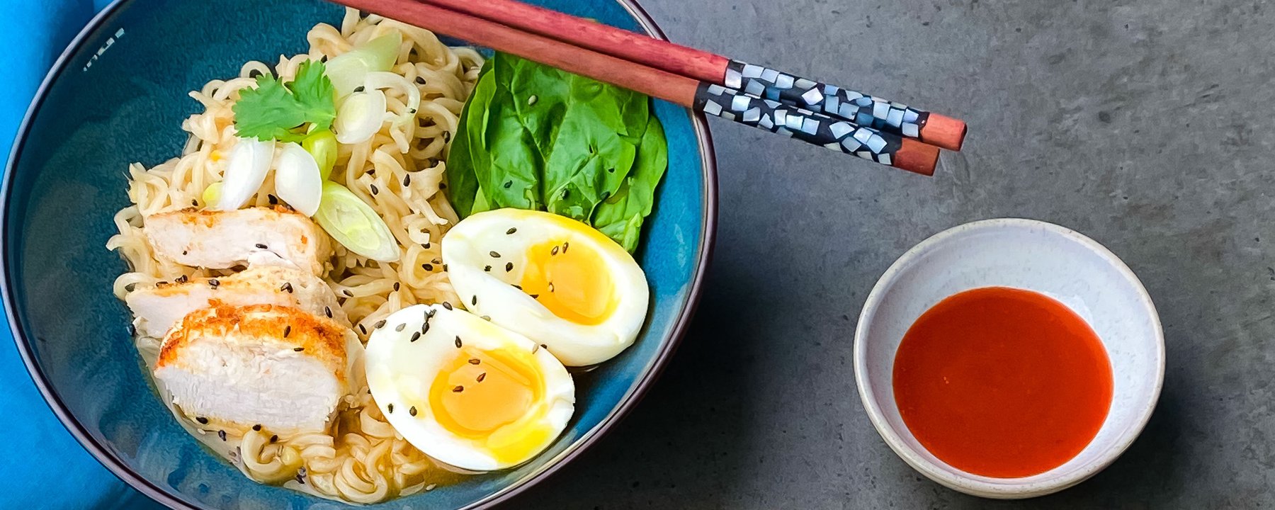 Bowl of ramen noodles topped with sliced chicken, soft-boiled eggs and green vegetables