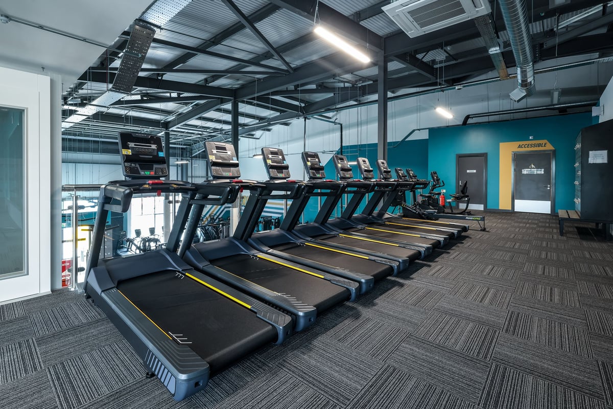 PureGym Bishop Auckland: Rows of modern treadmills in a dimly lit gym interior with industrial ceiling.